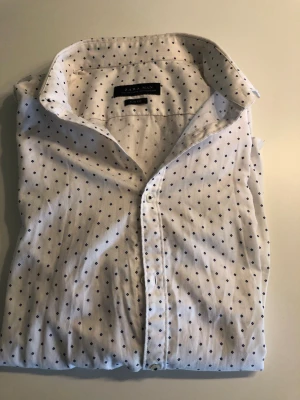 Vit prickig skjorta från Zara Man - Snygg vit skjorta från Zara Man med små svarta prickar och klassisk krage. Slim fit-modell med knappar framtill, perfekt för en stilren look. Tillverkad i mjuk bomull som känns skön mot huden.