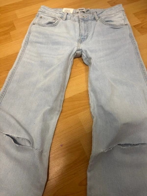 Low waist jeans - Säljer ett par ljusblå bootcut jeans med slitningar vid knäna. Är för små på mig och har kvar prislapp. Jeansen har klassisk femficksdesign och är tillverkade i denim med en snygg tvätt. Perfekta för en avslappnad och trendig look.