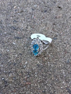 Silverring med blå stenar och kristaller - Snygg silverfärgad ring med tre blå droppformade stenar i mitten, omgivna av små klara kristaller i en oval form. Ringen har en elegant och glittrig design som verkligen drar blickarna till sig. Storlek 8 enligt märkning.