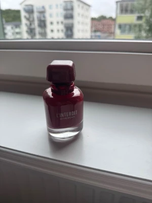 L'Interdit parfym från Givenchy - En elegant parfymflaska från Givenchy, L'Interdit. Flaskan är djup röd med genomskinlig botten och har en fyrkantig röd kork. Perfekt för dig som gillar exklusiva dofter och snygg design på parfymhyllan.