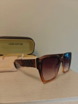 Bruna solglasögon - Snygga solglasögon med fyrkantig form och bruna bågar som tonar mot orange. Glasen är mörka och går i en gradient från svart till brunt.  Perfekt accessoar för soliga dagar. Jag ser inga repor på glaset. Köpta i Spanien ej i butik, inget märke