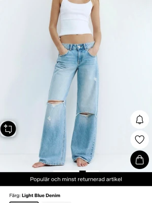 Ljusa vida jeans med slitningar - Säljer ett par ljusblå denimjeans med bred passform och slitna hål över knäna. Jeansen har hög midja, fem fickor och klassisk knappgylf. Perfekta för en avslappnad och trendig look.