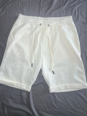 New Yorker shorts med snörning från ICONO - Säljer ett par vita shorts från ICONO i storlek XS. De har elastisk midja med snörning och sidofickor. Perfekta för sommaren och riktigt sköna tack vare det mjuka bomullsmaterialet. Enkla att matcha med allt i garderoben!