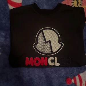 Svart tröja från Moncler - Säljer en svart tröja från Moncler med ett stort broderat logotypmotiv på framsidan. Tröjan har långa ärmar och ribbade muddar vid ärmslut och nederkant. Perfekt för en stilren look. S men passar som m också 