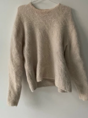 Beige fluffig stickad tröja H&M - Mysig beige stickad tröja från H&M i mohair- och ullblandning. Tröjan har en fluffig textur, rund halsringning och långa ärmar. Perfekt för dig som gillar en enkel men trendig look. Orginal pis 1200kr