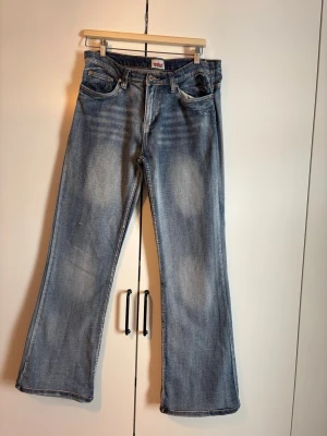 Blå bootcut jeans med broderade fickor - Säljer ett par ljusblå bootcut jeans med slitningar och snygga broderade detaljer på bakfickorna. Jeansen har klassisk femficksmodell och är tillverkade i denim. Perfekta för dig som gillar en avslappnad men ändå trendig stil.
