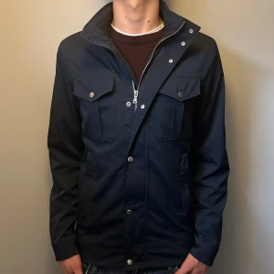 J.LINDEBERG JACKA - Snygg marinblå ”bailey poly jacket” från J.Lindeberg. Storlek S, men sitter som M! Den är som nyskick, inga defekter, nypris runt 3500. Skriv för fler funderingar 