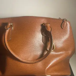 Ralph lauren väska. Ko-läder, original modell, bra skick, brun-färgad och guld-färgade detaljer. Med denna väskan kommer även ett extra handtag. Ungefär 40 bredd och 25 cm höjd.