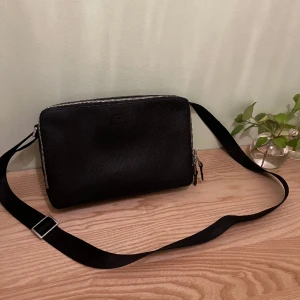 Lacoste Axelremsväska  - Hej! Skick 9/10 Ny pris ligger på 2 000 kr och säljs nu av mig för 1 149 kr!