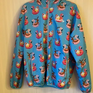 Flamingo Wind Jacket - Material: 100% Polyester.  Härligt mjuk och bekväm jacka.  Logotryck på bröstet Mjuk huva Två fickor med dragkedja Mjuk skaljacka med huva och två fickor. Skön tröja perfekt för dig. Inte mycket använd och inga skavanker.  Tvätt 30°C.