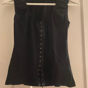 Svart topp - Svart kortärmad topp med snören och spännen i silver. I bomull och inga defekter