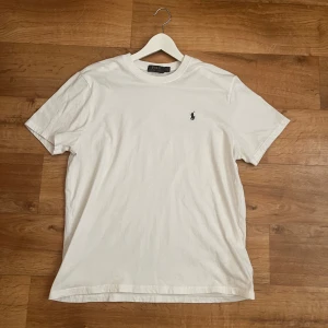 Vit t-shirt från Polo Ralph Lauren - En klassisk vit t-shirt från Polo Ralph Lauren med korta ärmar och rund halsringning. T-shirten har en broderad logotyp på bröstet. Hör gärna av er om ni har några frågor eller bud! 