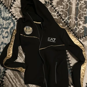 Guld EA7 Zip hoodid - Använt den 3ggr, väldigt sällsynt, går inte få tag på den. nypris 2200. väldigt bra skick, stl M