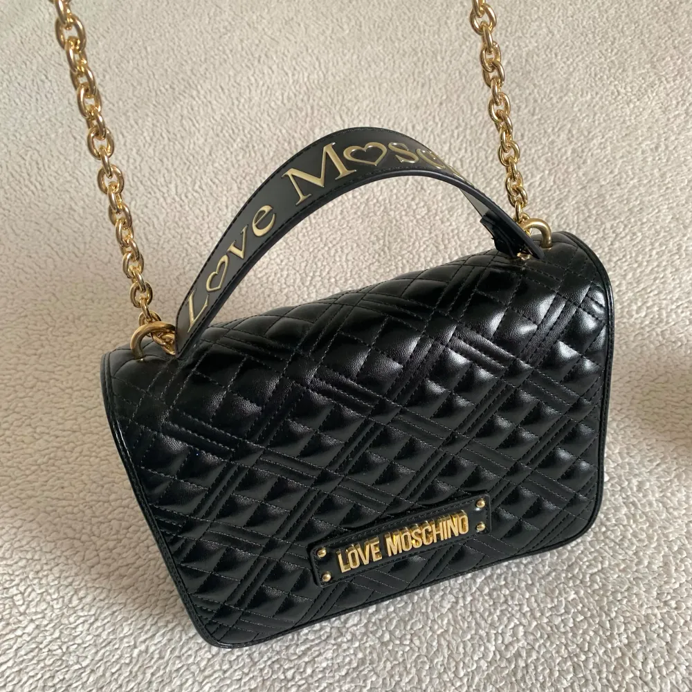 Axelremsväska från Love Moschino. Endast använd i några timmar och har bara legat i dustbag och dammat sedan dess. Helt nyskick, utan anmärkningar. Kvitto från Zalando finns. Ordinariepris 2095kr. Skickas med dustbag. . Laukut & Käsilaukut.