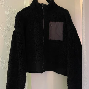 Teddy kofta - Säljer en croppad kofta typ i Teddy material från Nelly i strl XL,däremot ganska liten i storlek.  Finns även en ficka på ena sidan. 