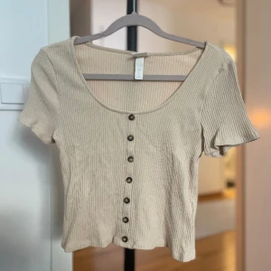 Beige kortärmad topp - Beige kortärmad och u-ringad topp med knappar framtill.