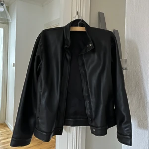 Fake skinnjacka - Svart fake skinnjacka, köpt på 2hand från början. Stel L men passar mig som är M. Lite oversized i modellen. Små slitningsmärken förekommer vid blixtlåsen (bild 3). Perfekt till våren. Hör av er vid frågor! 😊 Frakt inkluderad i priset. 