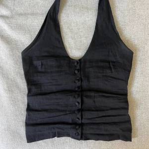 Partytopp - Svart bäst med knappar. Sitter som en halterneck topp. Strechig, passar fler storlekar. Tajt passform. Öppen i ryggen.