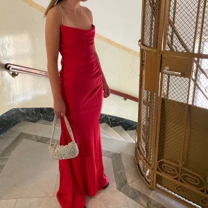 Röd balklänning - Säljer denna otroligt fina klänning från NA-KD, endast använd en gång, den går ner ända till marken på mig som är 175cm och Banden är i strass😍 Köpt för över 1000kr