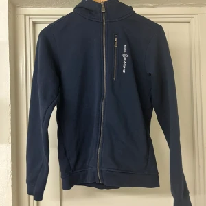 Sail Racing - En riktigt snygg marinblå zip hoodie från sail racing. Den är storlek 170 och i mycket bra skick eftersom att den nästan är oanvänd. Orginalpris 999kr.