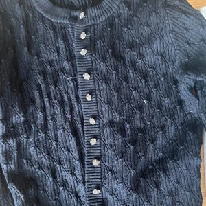 Svart stickad kofta från Zara - En elegant svart stickad kofta från Zara med ett unikt mönster och dekorativa knappar. Koftan har långa ärmar och en ribbad krage samt knappslå. storlek s men skulle säga mer som xs💓skriv för bättre bilder!