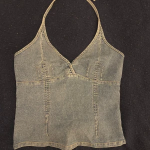 Snygg denim topp - Säljer denna supersnygga top i denim med halterneck ringning. Man kan knyta banden i nacken och dne har en dragkedja i sidan. I jättebra skick. 
