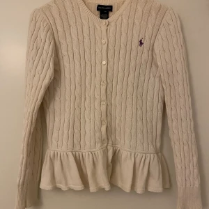 Ralph Lauren kofta, stl XL (barnstorlek) - En vit stickad Ralph Lauren kofta med volang kant längst ner i gott skick.   Frakt tillkommer, men kläder som köps kan samfraktas!