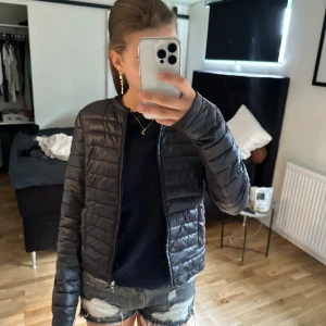 Svart pufferjacka från Guess - En svart pufferjacka från Guess med dragkedja framtill. Jackan är långärmad och har en quiltad design.