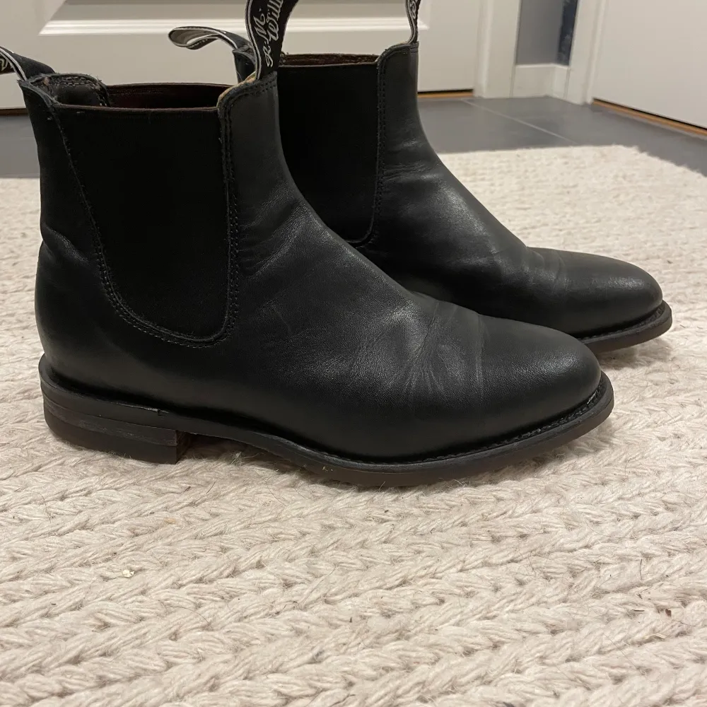 Ett par svarta Chelsea boots från R.M. Williams i skinn. Skorna har en oljeresistent sula och är i bra skick. De har elastiska paneler på sidorna och en dragflik baktill för enkel påtagning. Nypris 4 900 kr. . Skor.