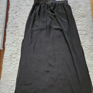 Svart långkjol -  Ny svart långkjol med elastisk midja. Kjolen är genomskinlig och har ett underkjol för extra täckning. slits på båda sidorna