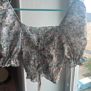 Blommig topp från Italian Style - En blommig topp från Italian Style med puffiga ärmar och volangdetaljer. Toppen har en åtsittande passform och är åtknytbar framtill.💖💖