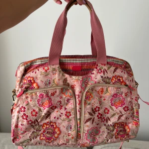 Väska Oilily - Säljer denna väskan från märket Oilily. Får plats med dator mm med många fack. Mycket fint skick, ngn fläck se bilder.