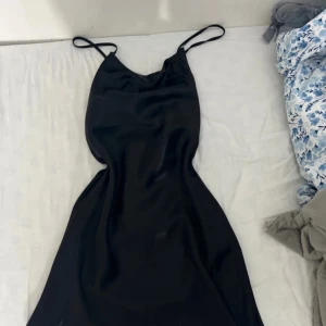 Svart satin klänning - Säljer denna oanvända svarta satinklänning med öppen rygg (cris-cross knytning) från Shein i storlek M 
