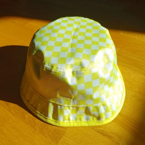 Buckethat, vändbar - En vändbar buckethat!😊 Ena sidan är svart med vit text och ljus gul kant. Andra sidan är gul med små rutor.Perfekt till sommaren!☀️Märket är vans. Unisex!💛