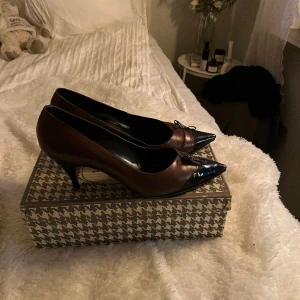 Brun svarta klackar med rosett - Asså så otroligt fina klackar som tyvärr är för stora för mig! Så fina med rosetten och blandningen mellan den svarta lackade främre delen och de bruna lädret, och pricken över i;et den söta rosetten. Bra kvalitet! Mellan 39,5 - 40