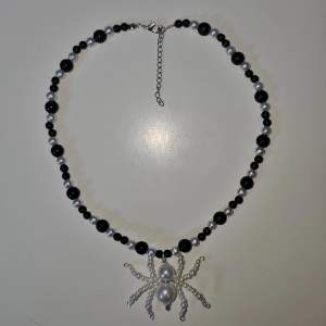 Handgjort halsband av mig i svart och vitt med en handgjord spindel. Halsbandet är gjort med plast pärlor, spindeln är också gjord med plast pärlor.