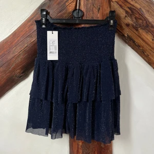 Neo Noir volangkjol - Neo Noir volangkjol i glittrig mörkblå färg, strl 36, helt oanvänd. 250kr