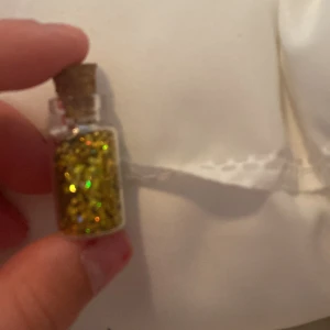 Guldglittrande ögonskugga i flaska - En liten flaska med kork som innehåller guldglittrande ögonskugga. Perfekt för att lägga till en glittrande touch till din makeup.