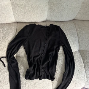 Svart ribbad kofta - En svart ribbad kofta med långa ärmar och sneda knappar framtill. ser lite nopprig ut på bilden men är inte alls så i verkligheten, jätte fin! 