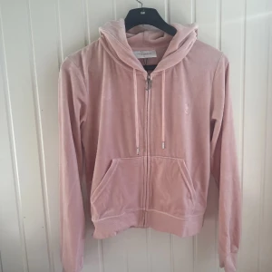 Rosa hoodie med dragkedja - En bekväm rosa hoodie med dragkedja framtill och två fickor. Hoodien har långa ärmar och en justerbar huva med dragsko.