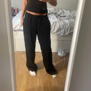 Svarta byxor - Ett par svarta byxor med elastisk midja och lös passform. Byxorna är långa och har en avslappnad stil, vilket gör dem bekväma för vardagsbruk.