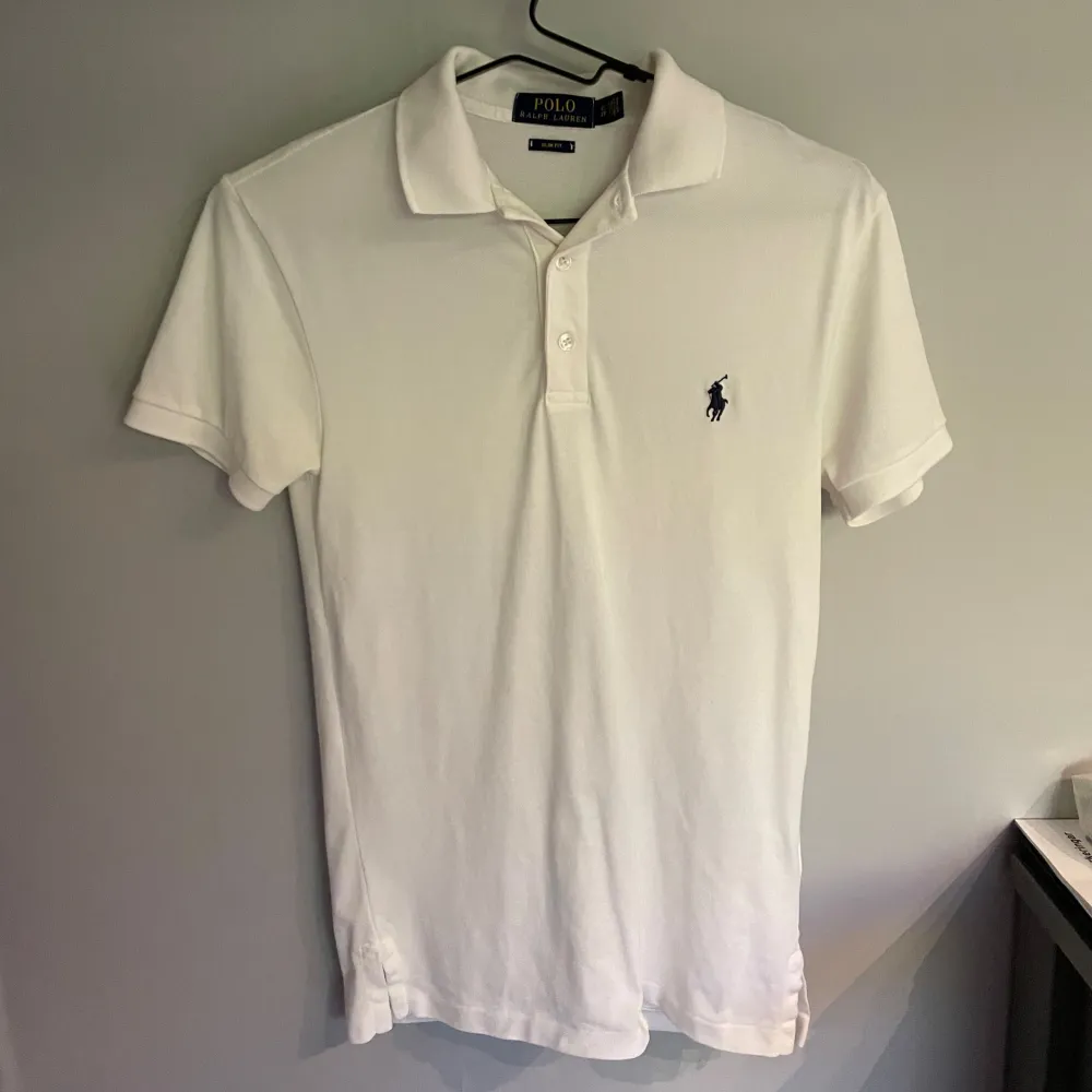 En stilren vit pikétröja från Polo Ralph Lauren i slim fit. Tröjan har korta ärmar och en klassisk krage med knappar. Den är dekorerad med Polo Ralph Laurens ikoniska broderade logotyp på bröstet. nypris 1500 kr, och den passar någon runt 170. hör av er för mer frågor/bilder.. T-shirts.