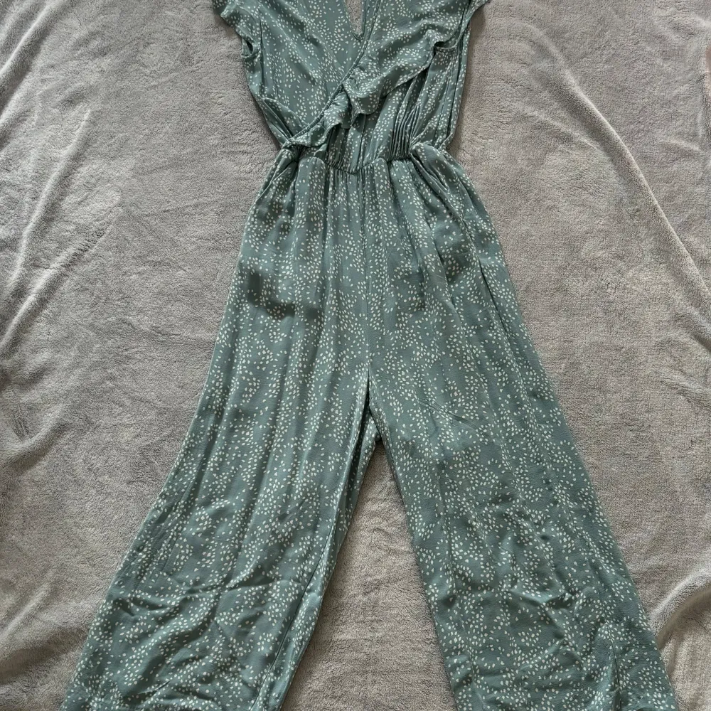 Detta är en grön- och vitfärgad jumpsuit. Jag vet tyvärr inte var den är köpt. Då jag har vuxit ur den väljer jag att sälja den. Den har två fickor på vardera sida av kroppen (se bilder). Jumpsuiten är i gott skick utan några defekter.. Mekot.