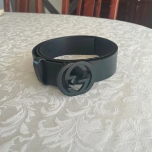 Gucci bälte i läder, storlek 95 modell 368186 BGH0V - Svart läderbälte med en stor, rund Gucci-logga i svart metall. Storlek 95 cm. Bältet är i gott skick och har inte använts mycket, mindre än 10 gånger. Inköpt på Selfridges i London i november 2018. Nypris 5100 kr. Finns ute på andra sidor också!