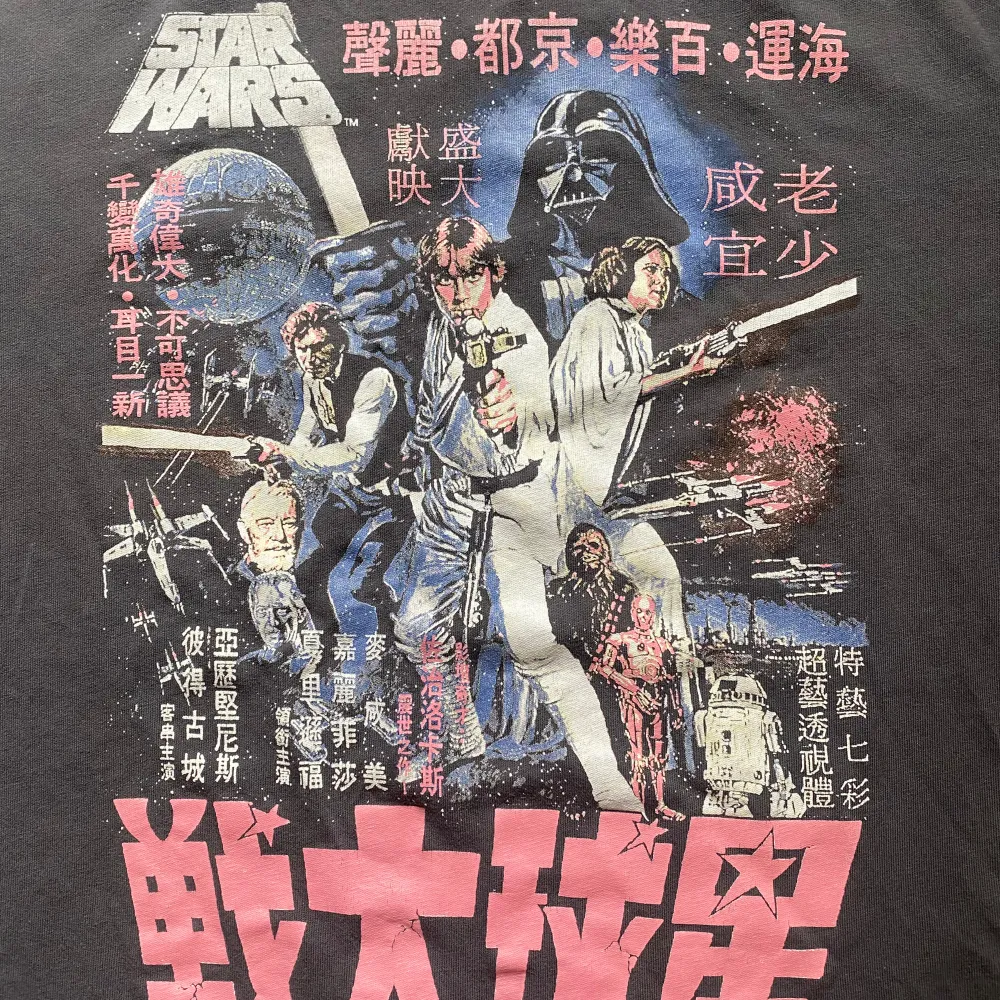 En mörk grå t-shirt med korta ärmar och ett färgglatt tryck av Star Wars i japansk stil. Trycket visar karaktärer från Star Wars-filmen och japanska tecken. 🌸. T-shirts.