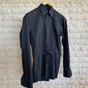 Svart skjorta - Svart skjorta från Bläck. Använd endast ett fåtal tillfällen, därav i gott skick. Säljes billigt pga. att jag ej använder plagget. 