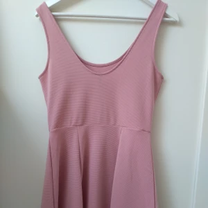 Rosa klänning från H&M Divided - En rosa ärmlös klänning från H&M Divided. Klänningen har en ribbad struktur och en rund halsringning. Den är av medellängd och har en enkel, elegant design.