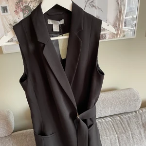 Ny kavajklänning i storlek 34 - Snygg svart kavajklänning med skärp i midjan. Klänningen har en krage och två fickor framtill. Ny med etiketten kvar. Väldigt snygg. Kommer från rökfritt och djurfritt hem. Storlek 34