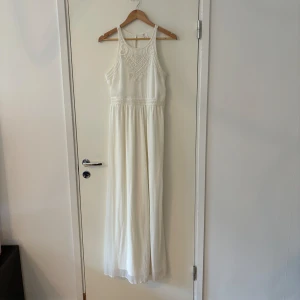 Vit långklänning med pärldetaljer - En elegant vit långklänning med detaljerade pärlbroderier på överdelen och midjan. Klänningen har en ärmlös design och en rund halsringning. Perfekt för festliga tillfällen.