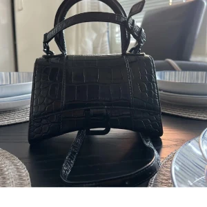 Balenciaga Hourglass XS Top Handle Bag, Black - Widht: 20 cm, Height: 12,5 cm Depth: 7,5 cm, Strap: 59 cm, Handle: 7 cm. Några repor på B:et och liiite missfärgningar. Pris går att diskutera!